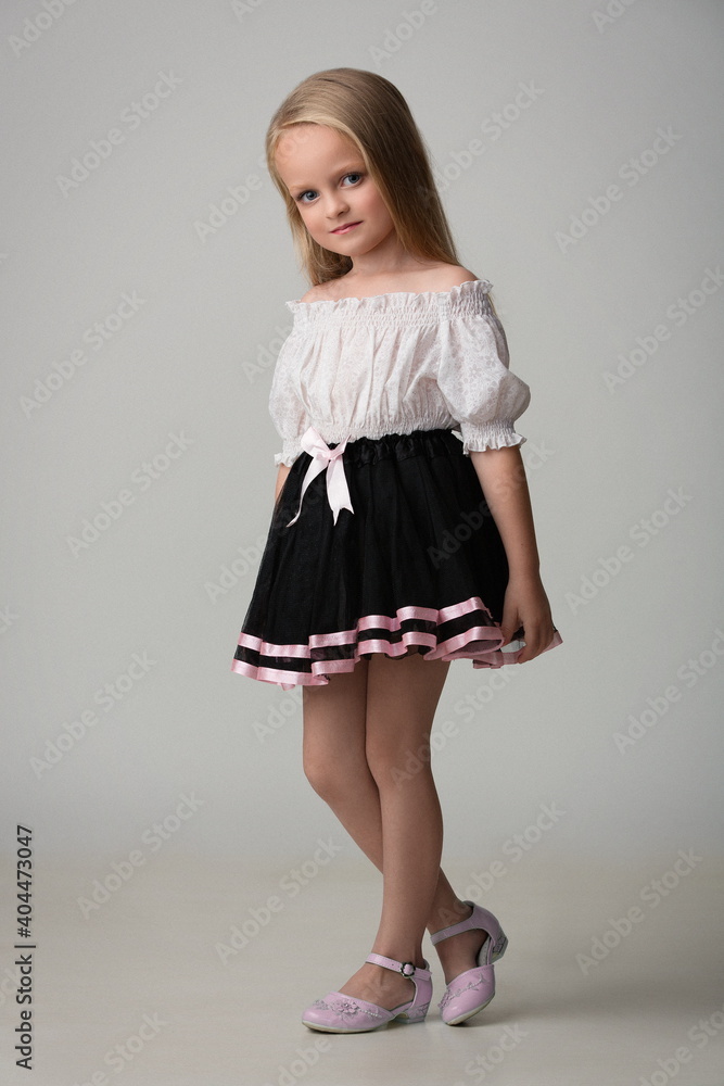 girl child with beautiful hair in a black skirt and white blouse on a light gray background girl child with beautiful hair in a black skirt and white blouse on a light gray background