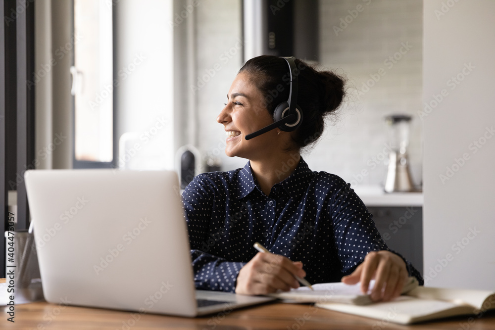 Happy young Indian woman in headphones study online on laptop look in distance dreaming or thinking. Smiling ethnic female in earphones have video call on computer. Distant education concept. Happy young Indian woman in headphones study online on laptop look in distance dreaming or thinking. Smiling ethnic female in earphones have video call on computer. Distant education concept.