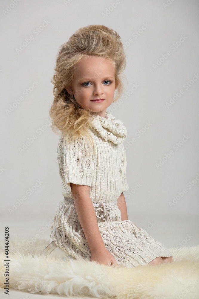 girl child with beautiful hair in a white knitted dress posing in sitting on a sheepskin skin girl child with beautiful hair in a white knitted dress posing in sitting on a sheepskin skin