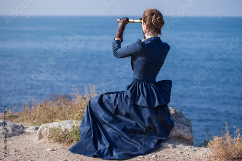 Romantic young beautiful lady looks at spyglass seascape. Vintage style. Steampunk concept.