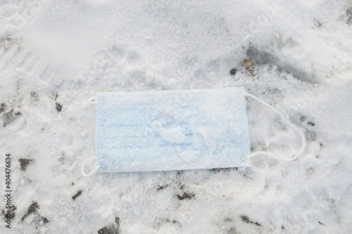 disposable medical mask with ear loops, sprinkled with snow on snowy ground