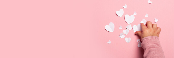 Child's hand takes a valentine card from paper on a pink background. Composition Valentine's Day. Banner. Flat lay, top view