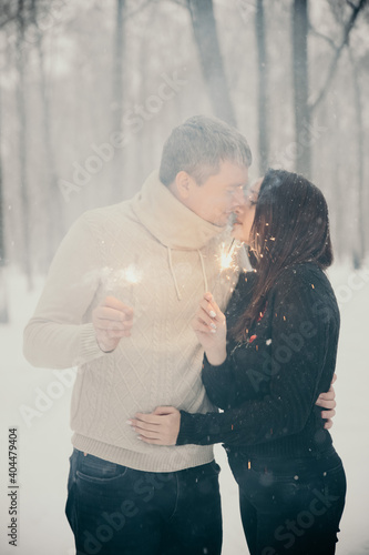 A man and a woman with sparklers on the background of a snow-covered forest in a snowfall