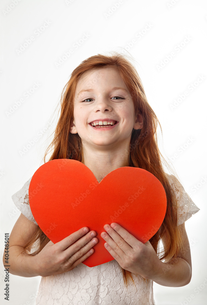 Portrait of laughing red-haired little girl holding big red heart in her hands on white background. Love, Valentines Day, Mothers Day or Fathers Day concept. Portrait of laughing red-haired little girl holding big red heart in her hands on white background. Love, Valentines Day, Mothers Day or Fathers Day concept.
