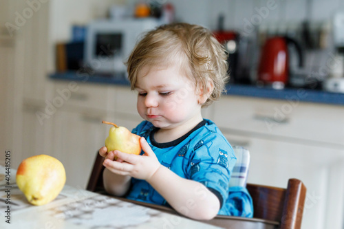 Cute adorable toddler girl eating fresh pear . Hungry happy baby child of one year holding fruit.