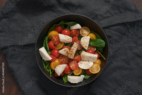 Salad with cherry tomatoes  spinach and mozzarella in black bowl on linen cloth