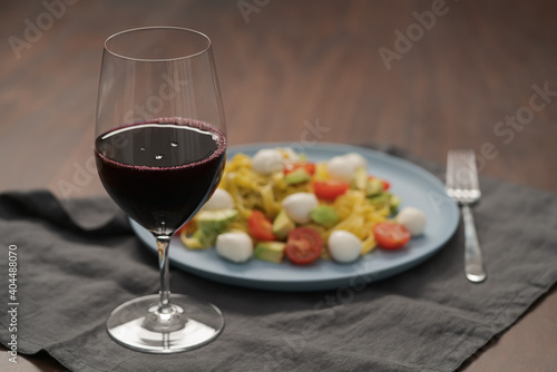 Red wine in thin wine glass with pasta on blue plate