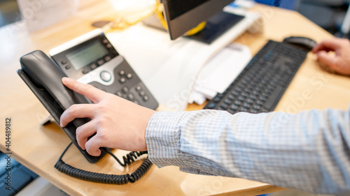 Male customer support operator hand trying to response customer call by using landline phone on working desk in office. Call center service and business communication
