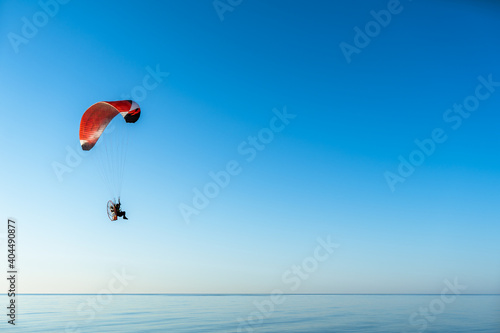 Motor paraglider fly over calm sea and at clear sunny day. Space for text.