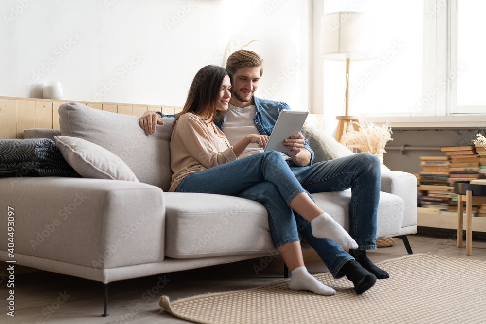 Young couple sitting on couch at home, using a tablet PC for Internet and social media. Young couple sitting on couch at home, using a tablet PC for Internet and social media.