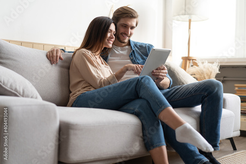 Young couple sitting on couch at home, using a tablet PC for Internet and social media.