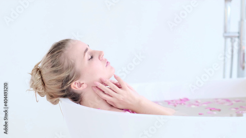 Beautiful Caucasian Blonde Girl In Bikini Lying In Flower Bath In Resort Day Spa Salon. Skin Care Therapy. Concept young woman relaxing in the bathtube.