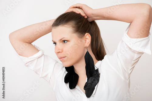 portrait of a beautiful young woman with her arms raised above her head presents black feather earrings on a white background
