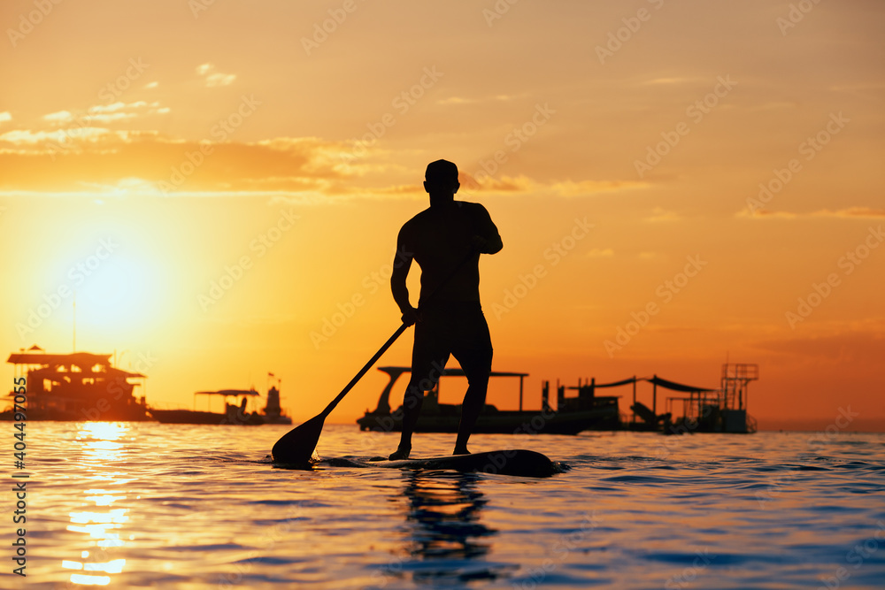 Active paddle boarder. Black sunset silhouette of young sportsman paddling on stand up paddleboard. Healthy lifestyle. Water sport, SUP surfing tour in adventure camp on family summer beach vacation.