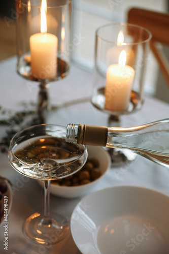 a drink is poured from a bottle into a glass on the table against the background of two candles