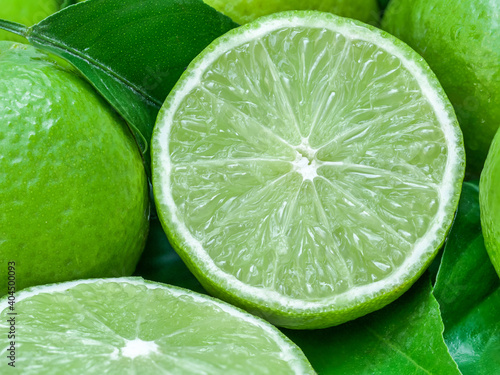 green lemons with half cut and leaves a sour fruit ingredient for healthy food and juice or beverage by closeup texture of limes for cuisine and nature background