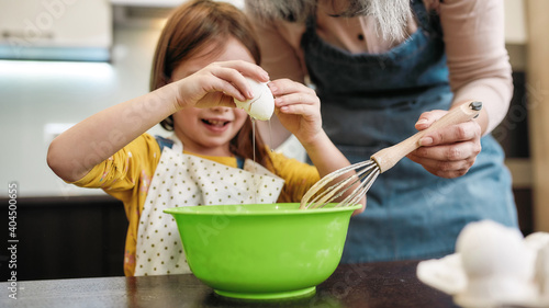 Photography Little girl cracking egg into large bowl near grandmother