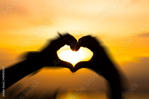 Holding hands as a heart with motion blur and golden sky on the background