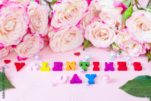 delicate bouquet of bushy peony roses  pearls and wooden colorful letters Valentines day on a pink background