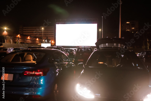 The best place to go. Many cars parked in front of a big white screen to watch movies or films sitting inside the car at drive in cinema in the evening