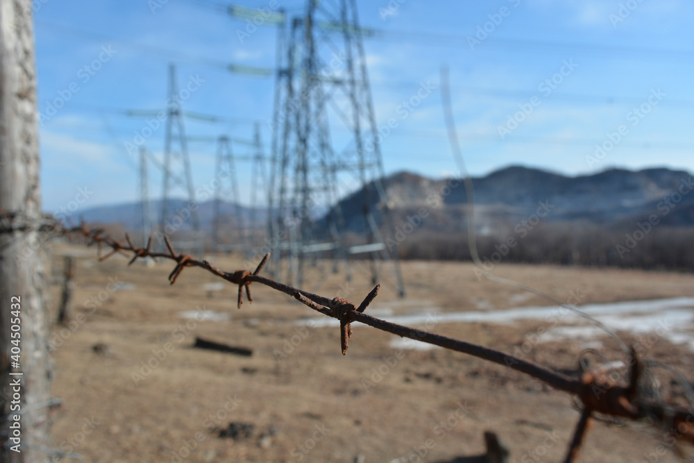 Rusty barbed wire in the foreground, blurred power lines and mountains in the background