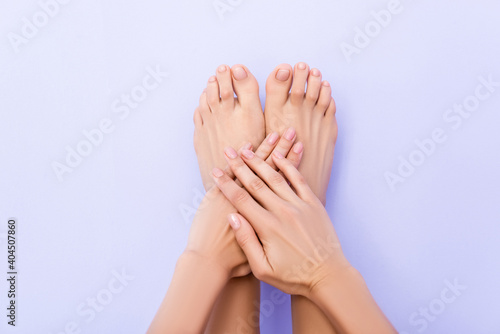 top view of female feet and hands with glossy nails on pastel purple background