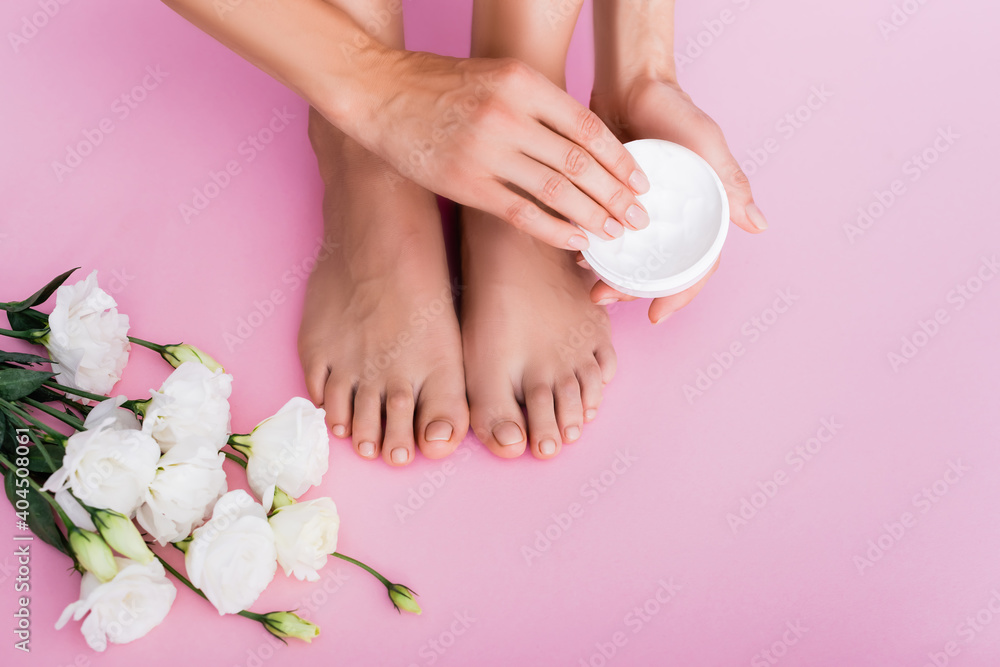 cropped view of barefoot woman holding cosmetic cream near white eustoma flowers on pink background cropped view of barefoot woman holding cosmetic cream near white eustoma flowers on pink background
