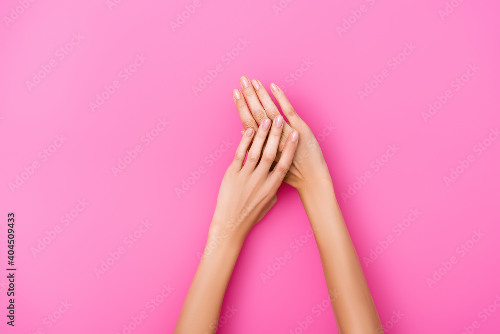 top view of groomed female hands with shiny nails on pink background top view of groomed female hands with shiny nails on pink background
