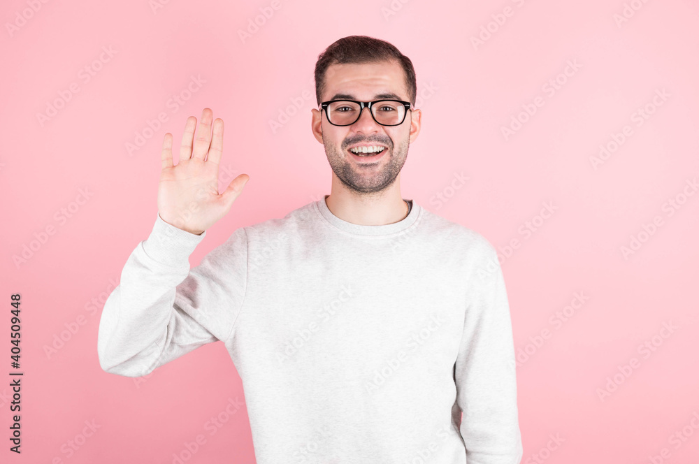 Naklejka premium Friendly positive smiling young caucasian male with stubble and dark hair in a trendy sweatshirt waving hand while greeting friends while having fun indoors. Human relationships and feelings
