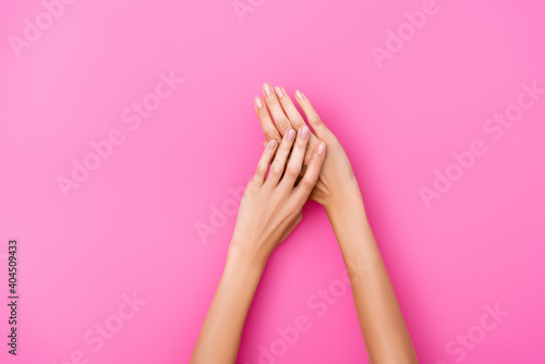 top view of groomed female hands with shiny nails on pink background