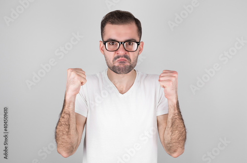 Young handsome latin man in casual t-shirt standing against isolated white background angry and mad  raising fists disappointed and furious  screaming in anger. Rage and aggressive concept.