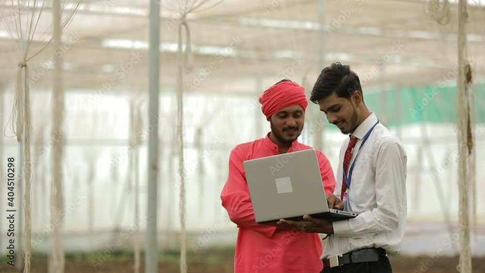 Young indian agronomist showing some information to farmer in laptop at greenhouse Young indian agronomist showing some information to farmer in laptop at greenhouse