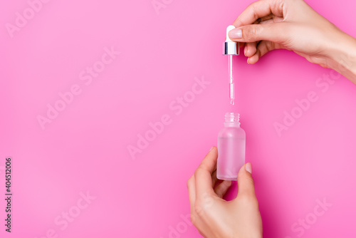 cropped view of woman holding bottle with cuticle remover and bottle on pink background