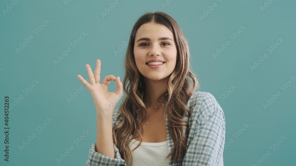 A pleased woman is doing ok gesture standing isolated over blue background A pleased woman is doing ok gesture standing isolated over blue background
