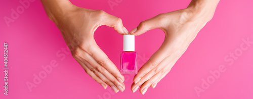 partial view of woman making heart sign with hands while holding vial of nail enamel on pink background, banner
