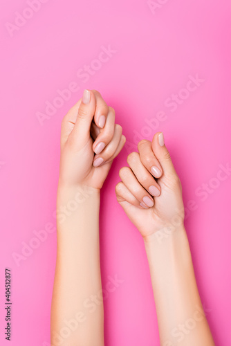 top view of groomed female hands with pastel manicure on pink background