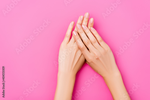 top view of groomed female hands with glossy fingernails on pink background