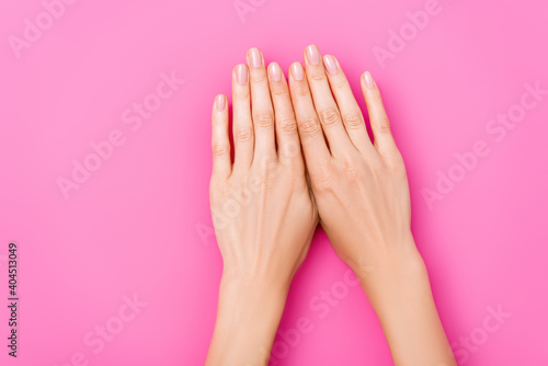 top view of female hands with pastel enamel on nails on pink background