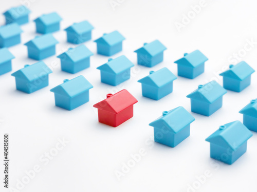Unique house different from group of same type miniature houses. Red house model among blue toy houses on white color background. Home choice or selection property and real estate. Property marketing