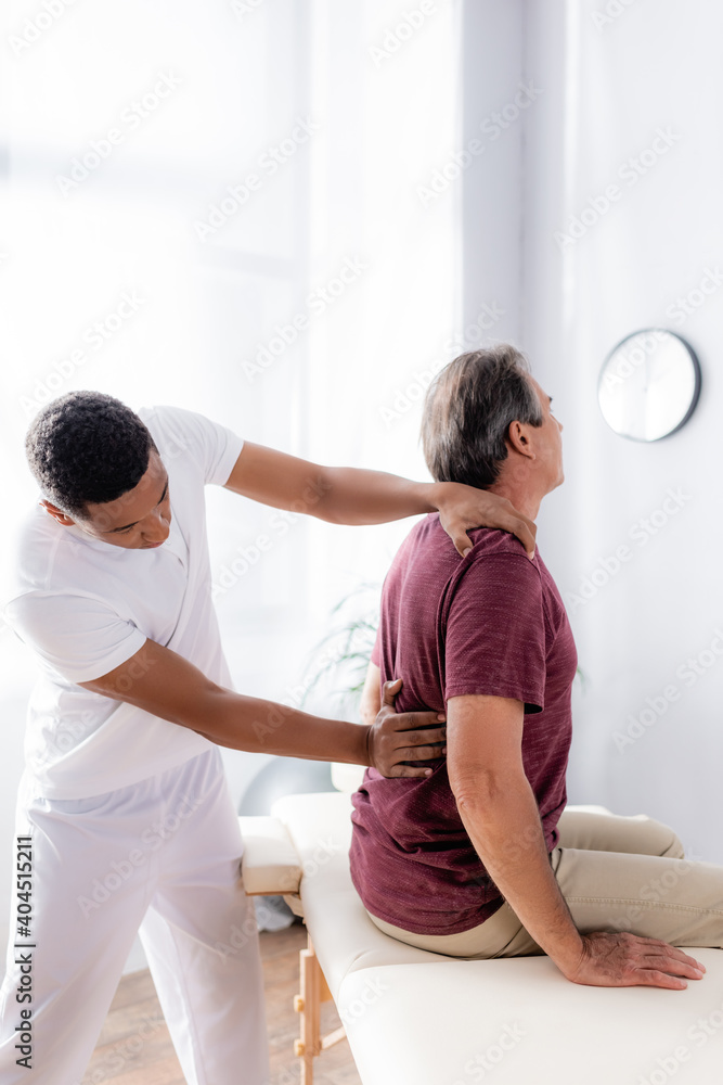 african american chiropractor working with back of middle aged man in clinic african american chiropractor working with back of middle aged man in clinic