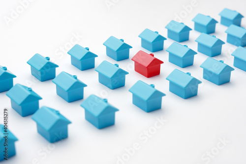 Real estate and property market in cottage village. Mortgage and buying a house. Red miniature house model among blue toy houses arranged in three rows different from group of same type miniature home