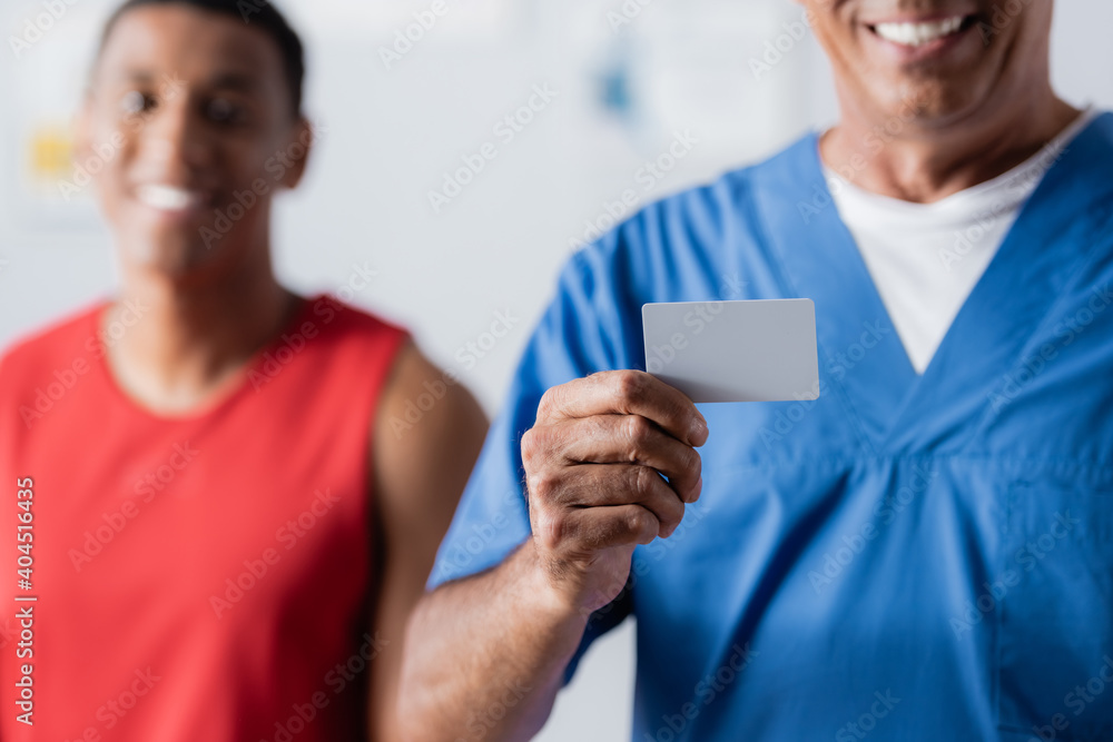 cheerful doctor holding blank card near african american patient in sportswear on blurred background cheerful doctor holding blank card near african american patient in sportswear on blurred background