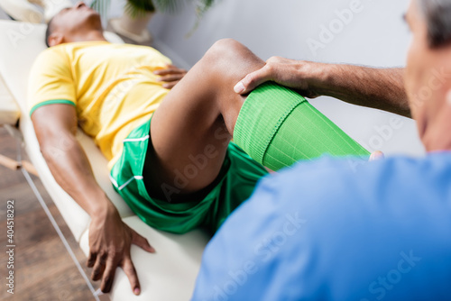 middle aged chiropractor working with injured african american sportsman in sportswear in clinic