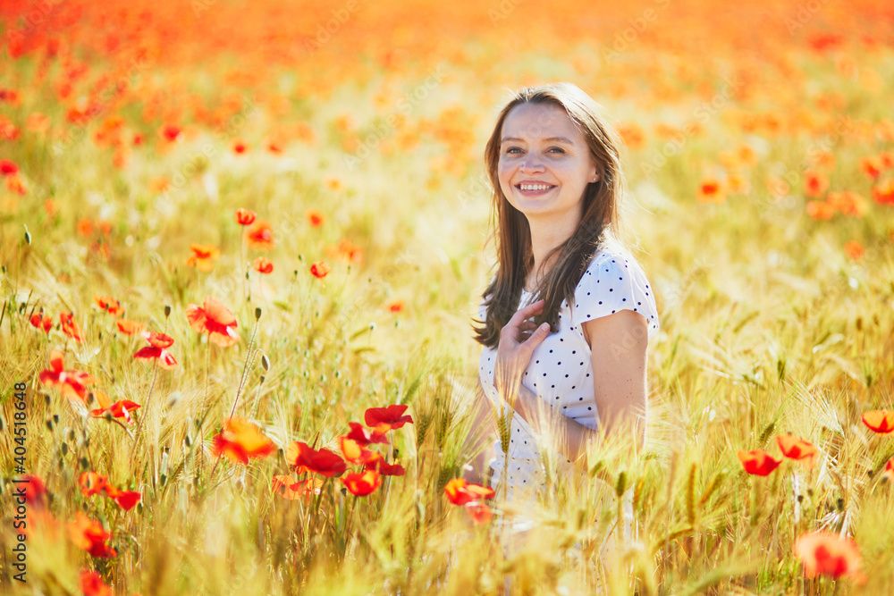 Beautiful young woman in white dress walking in poppy field on a summer day Beautiful young woman in white dress walking in poppy field on a summer day