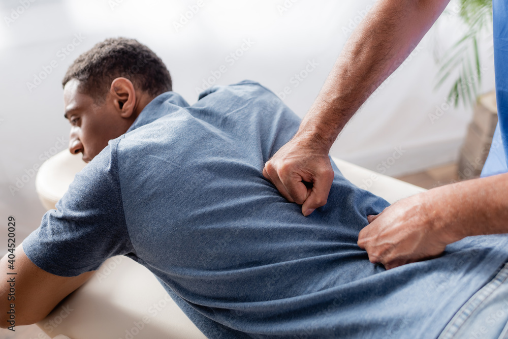 chiropractor working with young and injured african american patient on massage table in clinic chiropractor working with young and injured african american patient on massage table in clinic