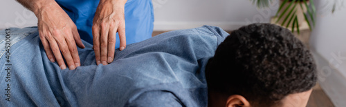 partial view of chiropractor working with young african american patient in clinic, banner