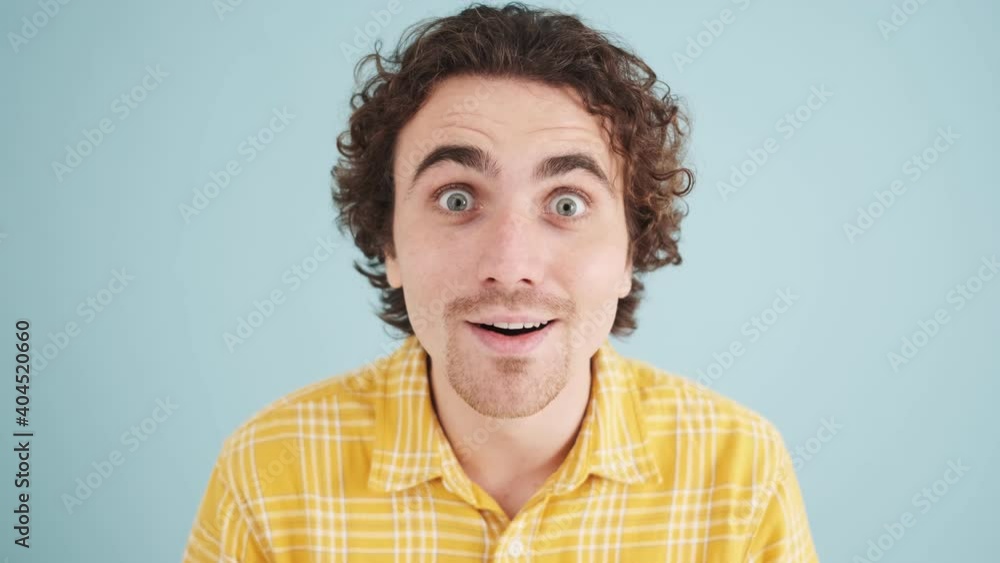 A surprised man is looking to the camera standing isolated over blue wall in studio A surprised man is looking to the camera standing isolated over blue wall in studio