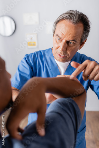 therapist pointing with finger at injured hand of african american patient on blurred foreground