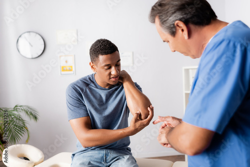 Photography injured african american man showing elbow to doctor in clinic
