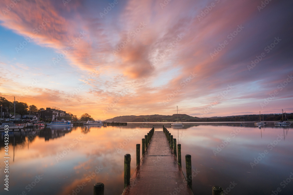 Peaceful colourful jetty sunrise with reflections by Windermere in the Lake District